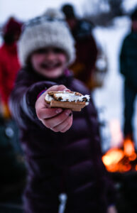 A Young Girl Offers A Cooked S'more Cookie To The Camera During A Visit To Tipi Camp On A Jackson Hole Vintage Adventures Sleigh Ride